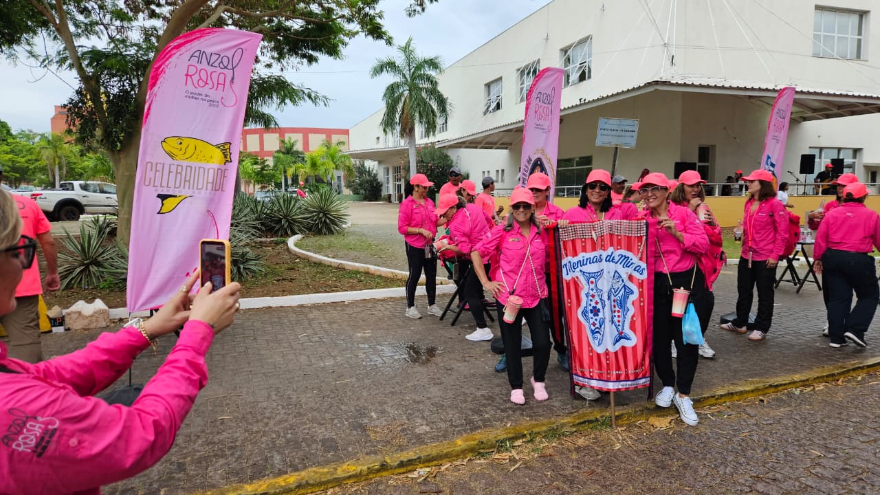 Mulher tira foto de outras mulheres vestidas de roupa de pesca na cor rosa.